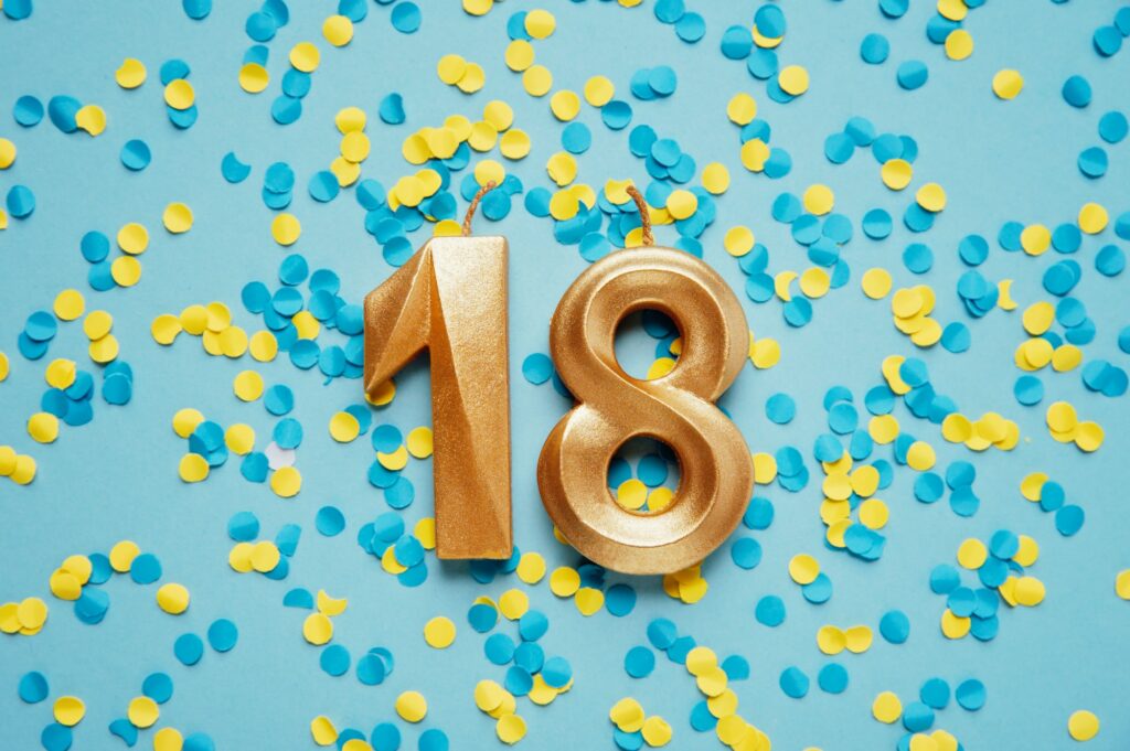 Number 18 eighteen golden celebration birthday candle on yellow and blue confetti Background.